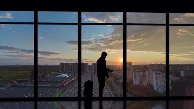 详情图-在清晨的城市背景下，提着箱子的男子站在室内。时间流逝