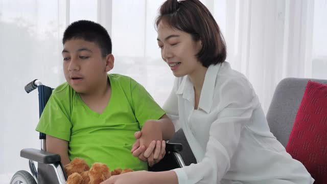 亚洲家庭母亲手牵手拥抱残疾的儿子在家里的轮椅上