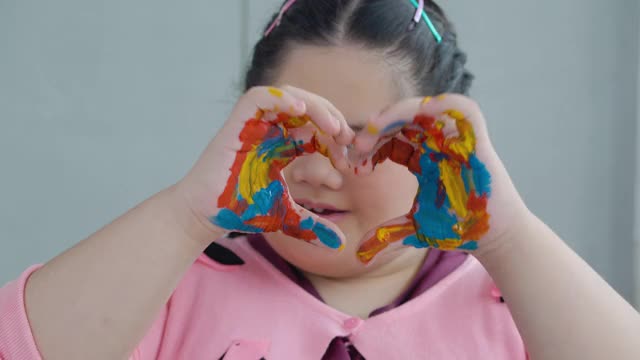 肖像的亚洲小女孩15岁微笑与唐氏综合症看着相机，而手画在彩色油漆。不同的残疾人肖像概念。