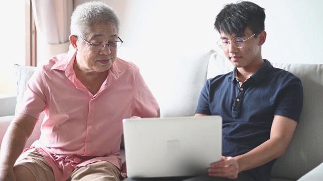 亚洲华人老人看笔记本电脑检查信息社交媒体冲浪与他的孙子