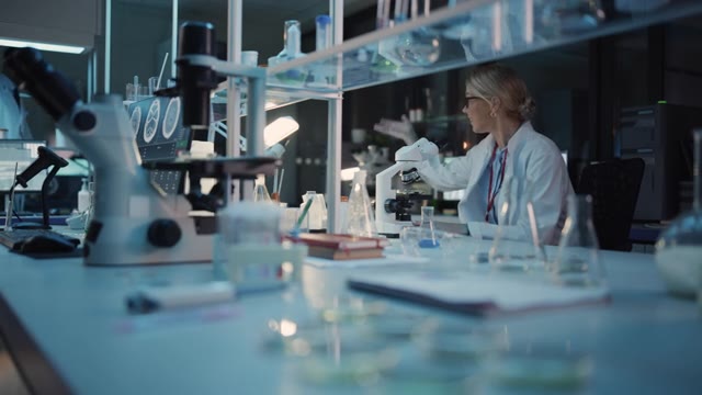 详情图-女性研究科学家在显微镜下研究病毒疫苗样本时取得重大发现。她打电话给同事，并与其他生物工程师分享她的成功。
