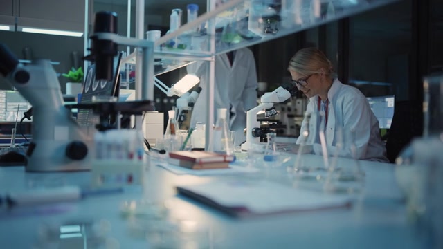 详情图-女性研究科学家在显微镜下研究病毒疫苗样本时取得重大发现。她打电话给同事，并与其他生物工程师分享她的成功。