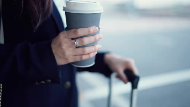 投资者女士拿着咖啡杯在机场出发区等待机场班车