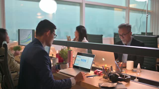亚洲华裔年轻商人在办公室里工作，在他的工作场所用笔记本电脑做他的报告