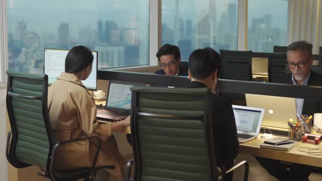 4名成熟的亚洲华人白领在他们的办公室工作和交流