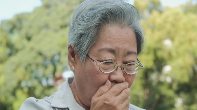 老年妇女在公园咳嗽。