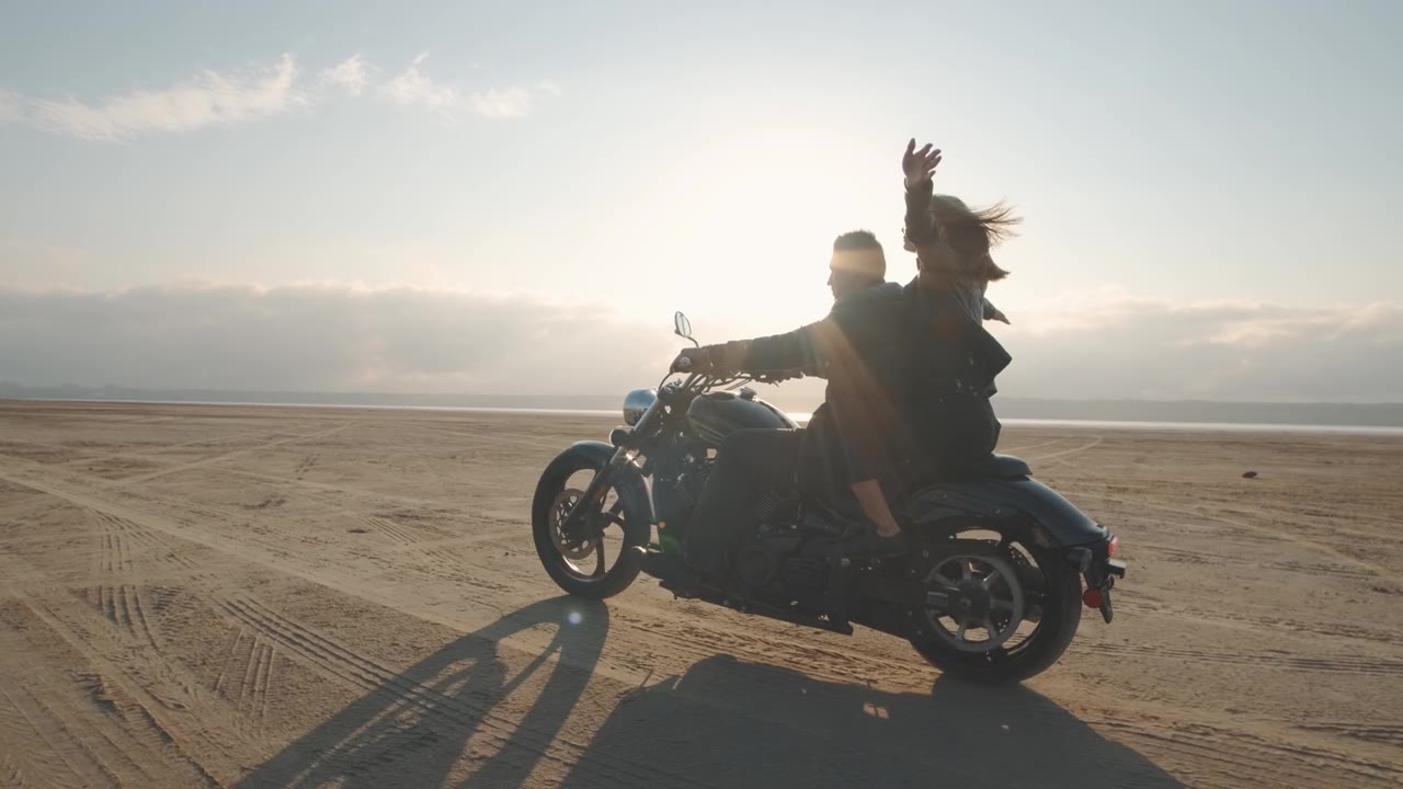詳情圖-一個男的和一個女的在沙漠里騎摩托車。一對相愛的情侶騎著摩托車在干涸的鹽湖上享受日落時分的美好時光。慢動作鏡頭