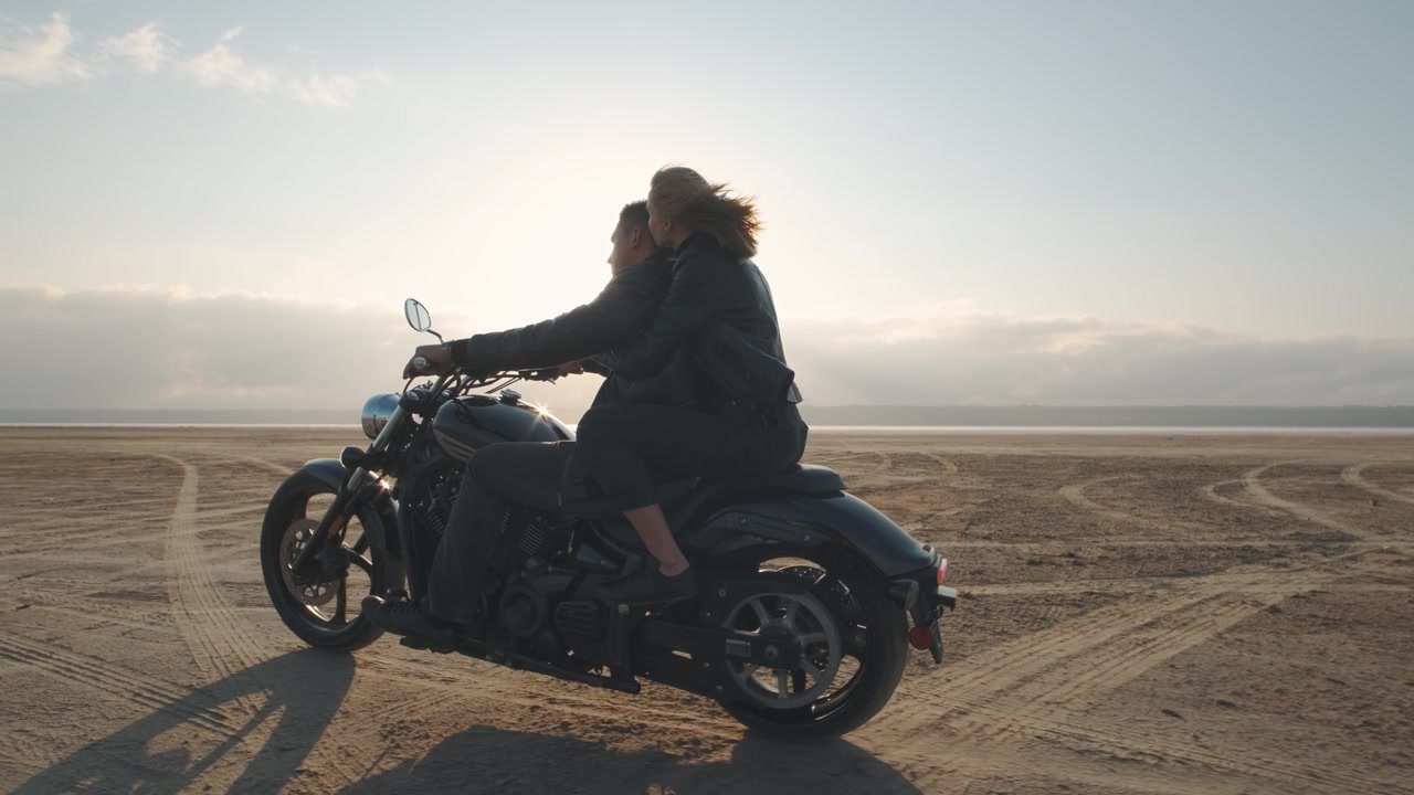 詳情圖-一個男的和一個女的在沙漠里騎摩托車。一對相愛的情侶騎著摩托車在干涸的鹽湖上享受日落時分的美好時光。慢動作鏡頭