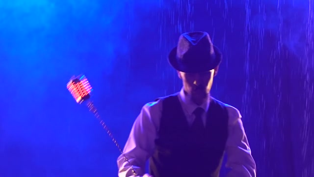 詳情圖-時(shí)髦的男人用發(fā)光的手榴彈表演火力特技。藝術(shù)家在藍(lán)色煙霧繚繞的演播室背景下，在雨流中表演。展示光和水。用慢動(dòng)作拉近鏡頭