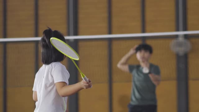 亚洲华人女羽毛球教练在羽毛球场上教她的学生