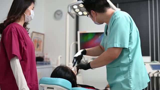 一名亚洲华人牙医在诊所护士的帮助下为他的病人做手术