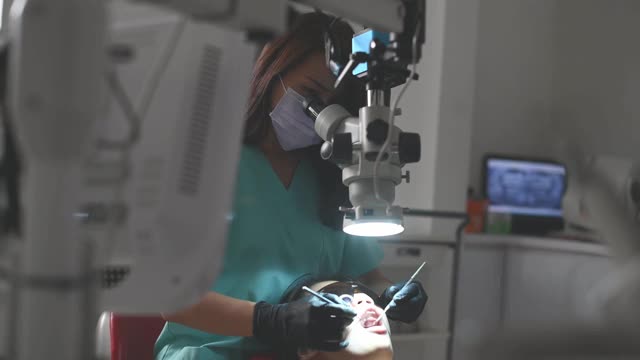 亚洲华裔女牙医在牙医办公室里用显微镜观察病人的牙齿