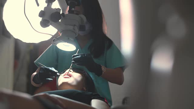 亚洲华裔女牙医在牙医办公室里用显微镜观察病人的牙齿