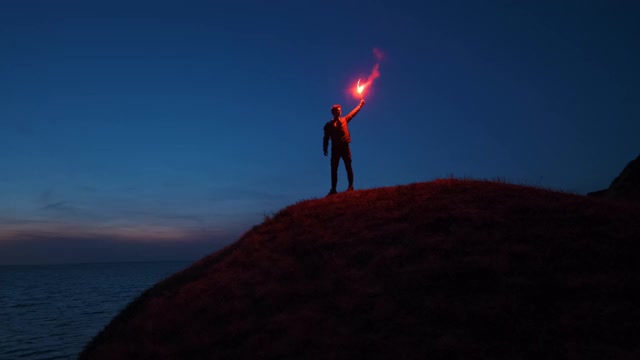 那个拿着一根火棒的人站在海边的山顶上。慢动作