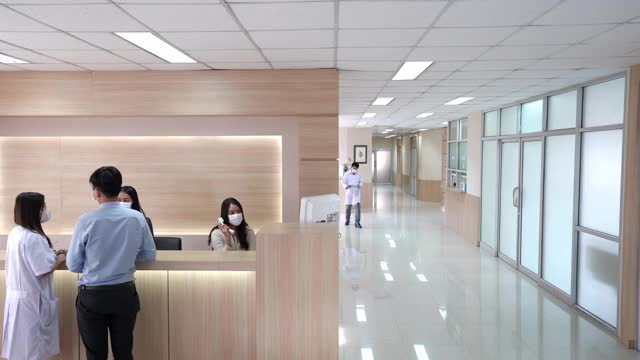 4K宽镜头的大堂等候区在现代化的医院或医疗设施，病人在询问柜台和一组专业医生和护士在医疗中心的卫生服务。