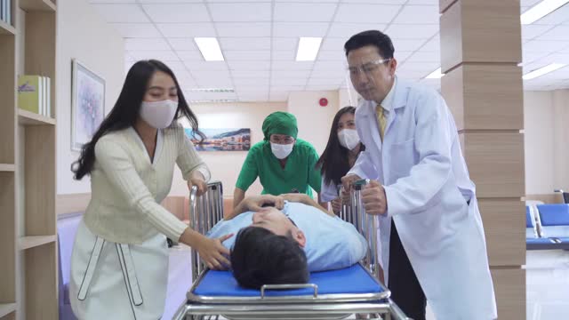 亚洲专业医生与外科医生和病人家属在担架上奔跑和移动昏迷的男性病人通过医院大厅到手术室。医疗保健服务理念。