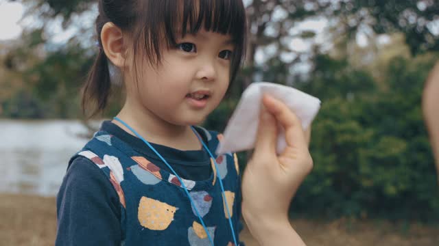 母亲拿着纸巾，帮助生病的女儿擦鼻子
