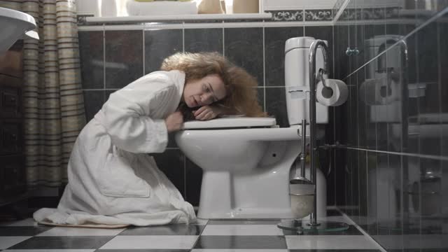 病人或孕妇打开厕所呕吐的侧视图。不健康的白人女士在浴室白色浴衣的广角镜头。中毒或怀孕的概念