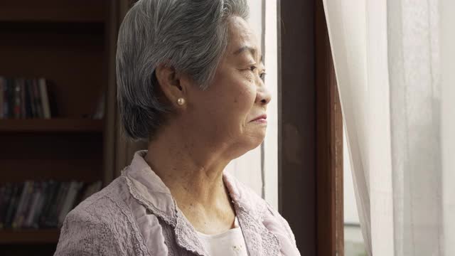 老人在家安慰和支持站在窗边的抑郁妇女。从背后扶着妻子的肩膀安慰她。