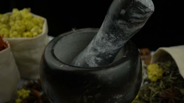 香草和花朵用杵缓慢地落进花岗岩臼里。健康有机食品、中草药、天然护理、芳香疗法和有机化妆品理念。