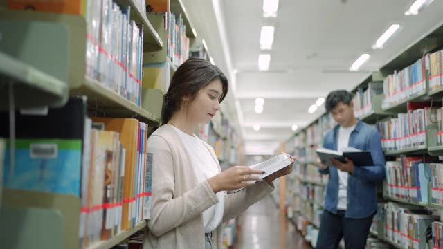 聪明的亚洲男女大学生读书之间的书架与校园图书馆的拷贝空间。