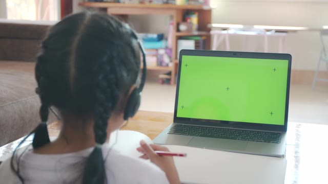 详情图-亚洲女童学生戴上耳机，通过视频电话与老师在线学习。由于Covid,-,19大流行，在隔离期间，孩子正在用电脑笔记本电脑在家学习。