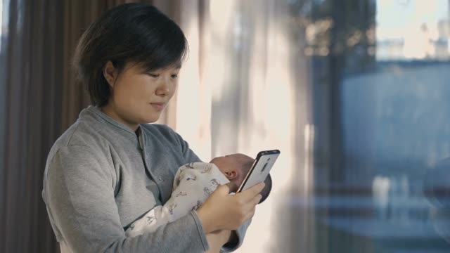 妈妈一边抱着孩子一边使用智能手机