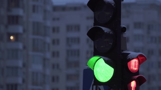 详情图-下雪的夜晚，城市街道上的交通灯。特写镜头。冬天建筑物背景上的红绿灯