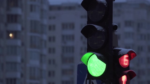 详情图-下雪的夜晚，城市街道上的交通灯。特写镜头。冬天建筑物背景上的红绿灯