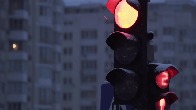 详情图-下雪的夜晚，城市街道上的交通灯。特写镜头。冬天建筑物背景上的红绿灯