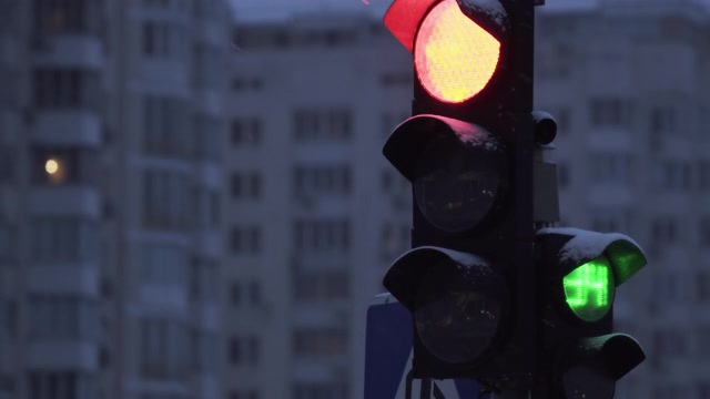 详情图-下雪的夜晚，城市街道上的交通灯。特写镜头。冬天建筑物背景上的红绿灯