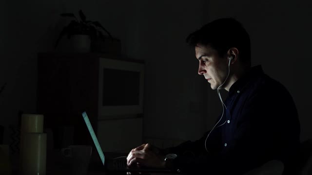 千禧一代严肃的年轻人在家里办公，一边用耳机在笔记本电脑上打字一边远程工作——科技社交距离概念