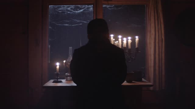 成熟的男人凝视着夜晚的窗景。有烛光的暗室