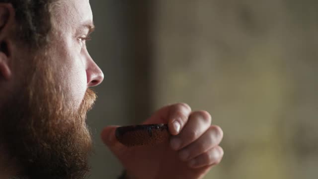 一幅留着胡子的嬉皮士男子用陶碗喝中国茶的肖像。中国茶道
