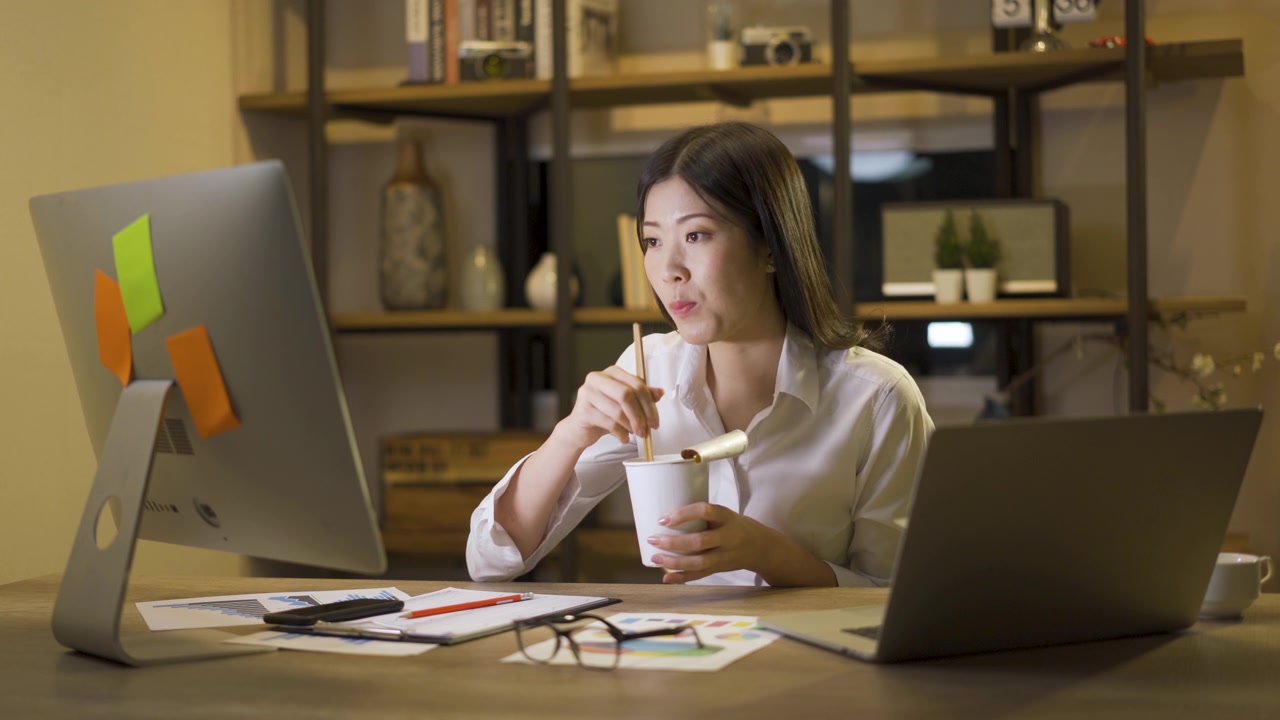詳情圖-亞洲自由職業(yè)者精明的商業(yè)女性一邊吃著方便面，一邊在家里的客廳里用筆記本電腦工作。