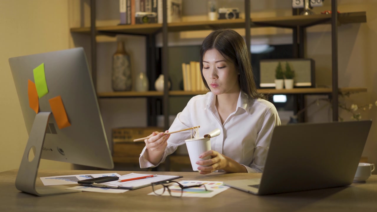詳情圖-亞洲自由職業(yè)者精明的商業(yè)女性一邊吃著方便面，一邊在家里的客廳里用筆記本電腦工作。
