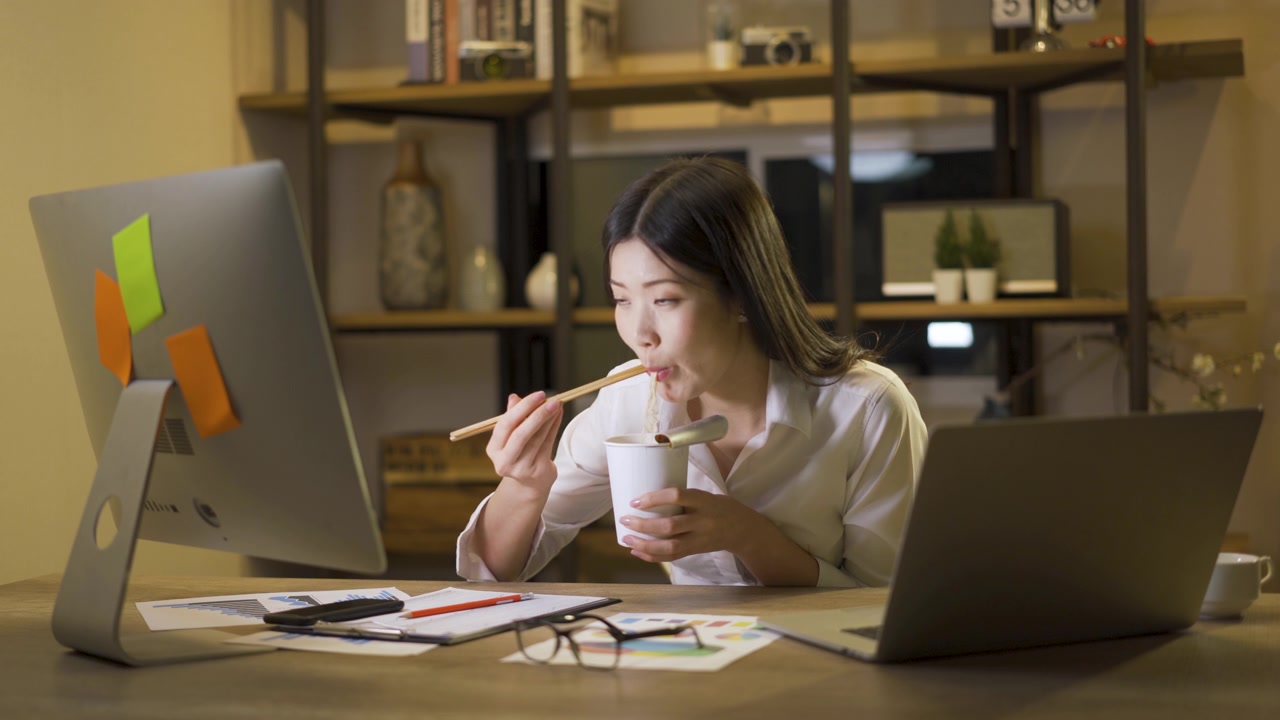 詳情圖-亞洲自由職業(yè)者精明的商業(yè)女性一邊吃著方便面，一邊在家里的客廳里用筆記本電腦工作。