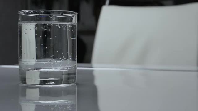 白色的餐桌上放着一杯矿泉水，用玻璃酒杯喝水。