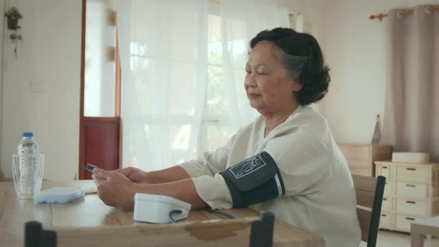 老年妇女自己用数字压力表测量血压和心率，并在家里用平板记录测试结果。