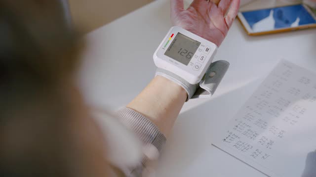 高级成人手腕监视器检查血压记录她的血压数字在笔记本上