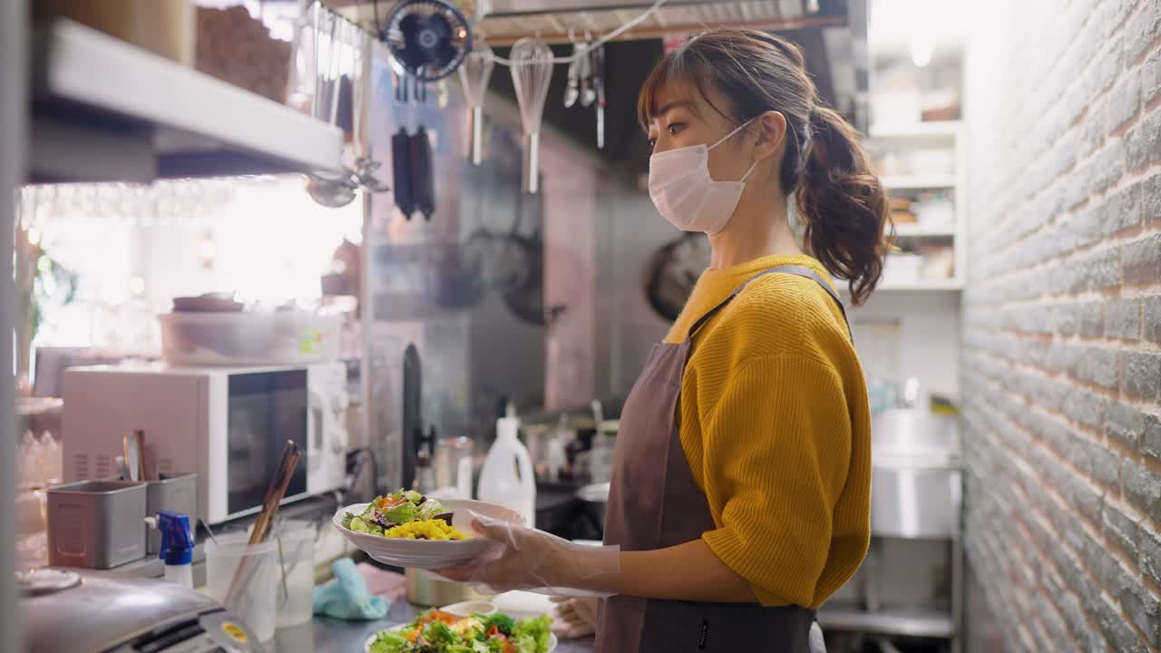 女厨师在café和餐厅的商业厨房给女服务员递食物