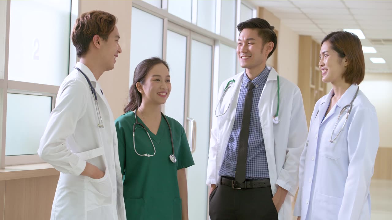 詳情圖-圖為，亞洲男性和女性醫(yī)生站在一起談?wù)撝委煵∪说氖虑楹螅⑿χ徊骐p臂望著攝像機(jī)的照片。醫(yī)生在休息時間聊天。