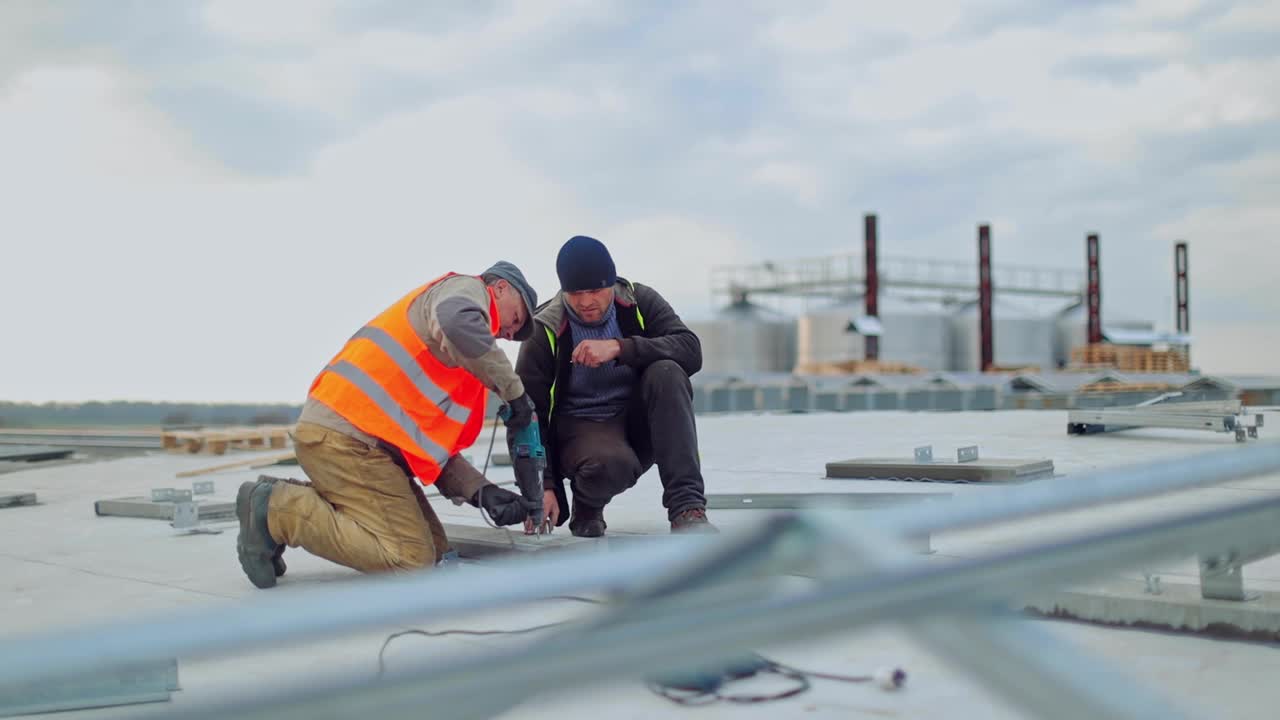 太阳能技术人员使用钻机在太阳能农场工作。工人们正在屋顶上安装太阳能光伏板，将太阳能转化为电能。