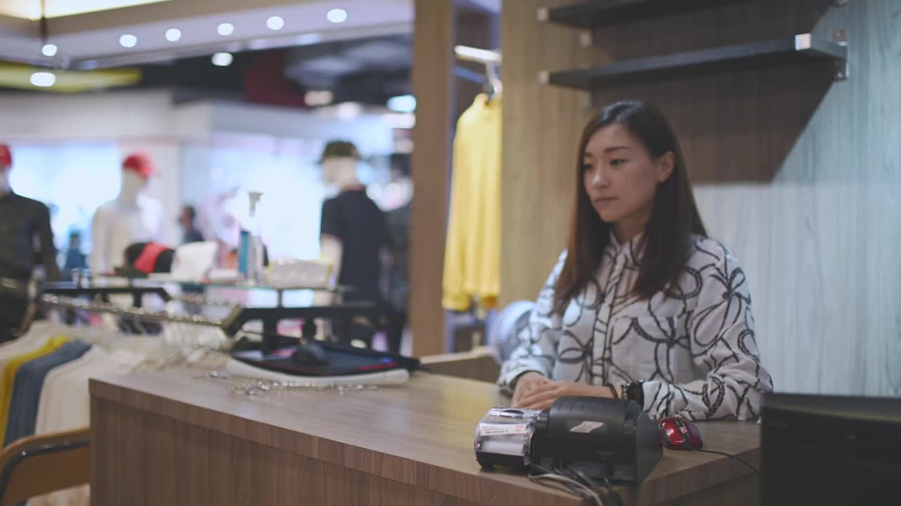 亚洲华人精品店老板接受信用卡从她的客户在收银员结账在男装店