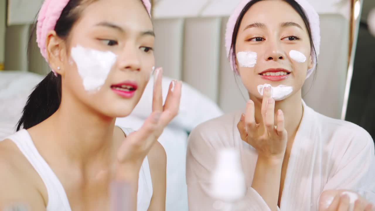 亚洲两个年轻的女性放松水疗在家里一边笑一边放松，微笑的女孩朋友有乐趣。居家。年轻女子在脸上敷面膜。水疗中心提供各种健康治疗。