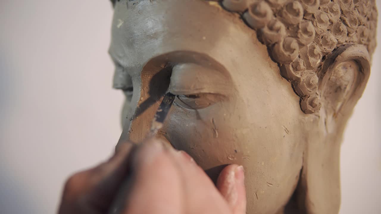 泥塑佛像的人像面，艺术家用刮刀打磨细节
