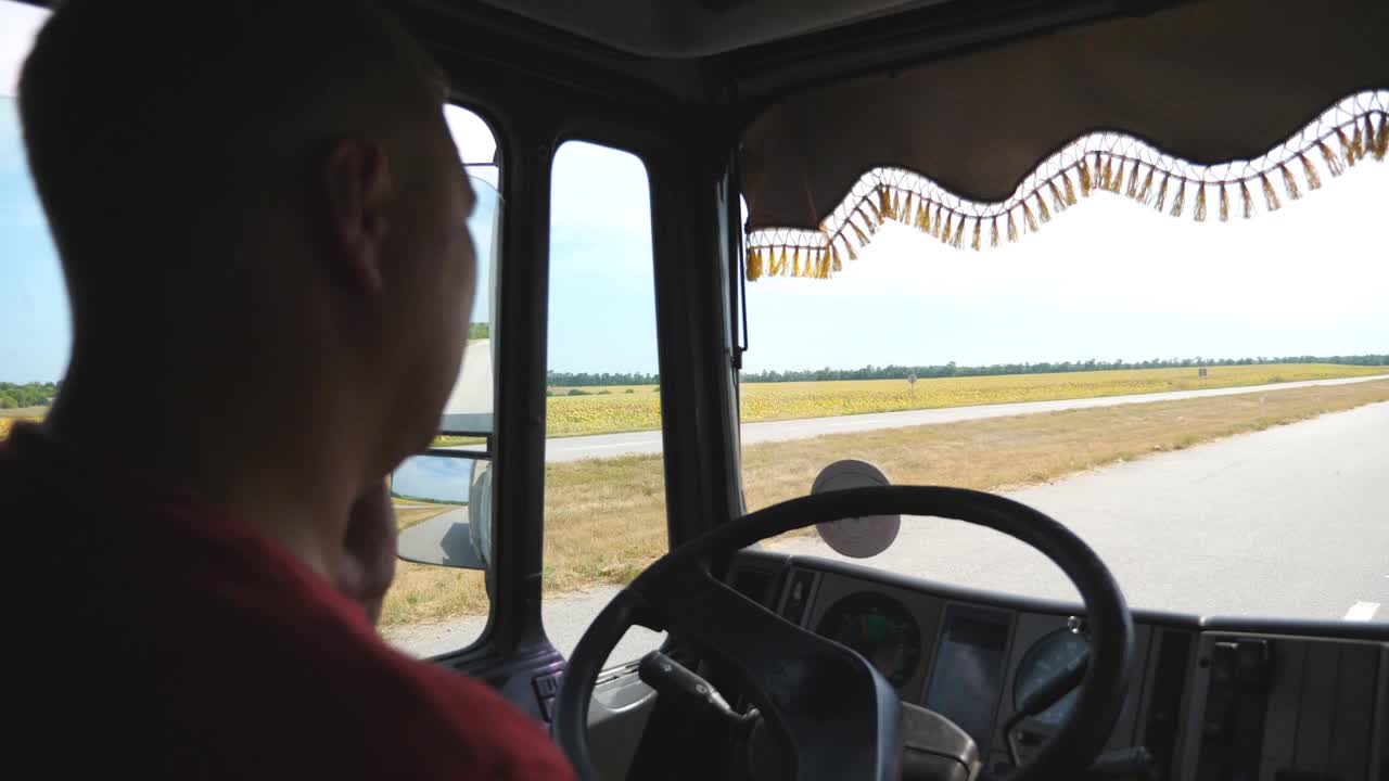 卡车司机在乡村公路上驾驶卡车时用智能手机说话。一名男性卡车司机一边开车穿过乡村一边打电话。物流的概念。后视图慢动作