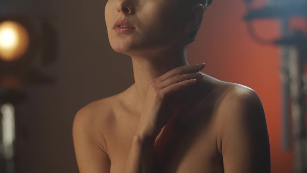 黑发女孩女演员美丽的眼睛化妆在明亮的光，移动缓慢，触摸她的脖子与她的手和直视前方。