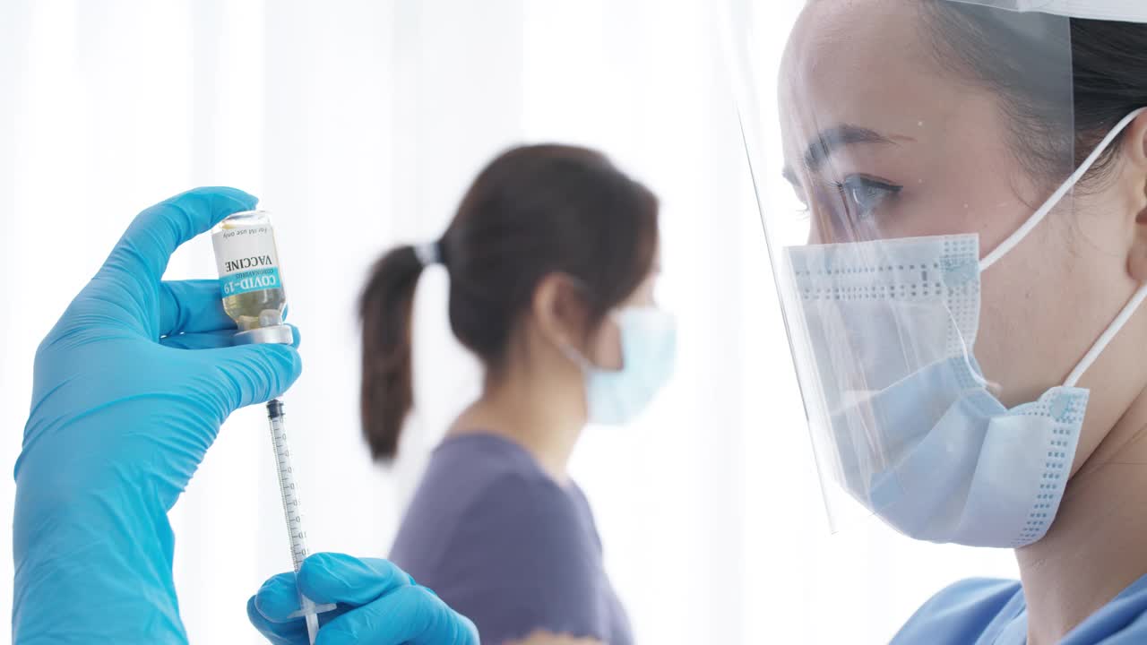 年轻的亚洲女性医生或擦洗护士手持注射器冠状病毒疫苗小瓶准备注射亚洲志愿者成熟的成年女性在医疗保健医疗保护和预防新冠肺炎的概念。