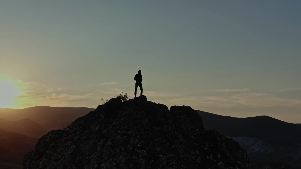 一个人的剪影站在山顶的夕阳在山中饮水。太阳的光线通过山顶和旅行者的脚。鸟瞰图。